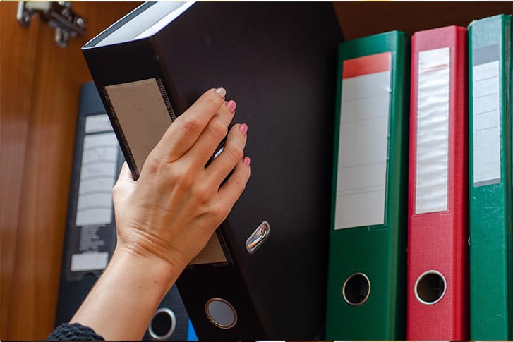 Adult pulling a large binder of papers off a shelf.
