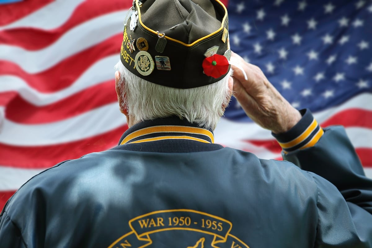 An elderly veteran salutes the American flag.