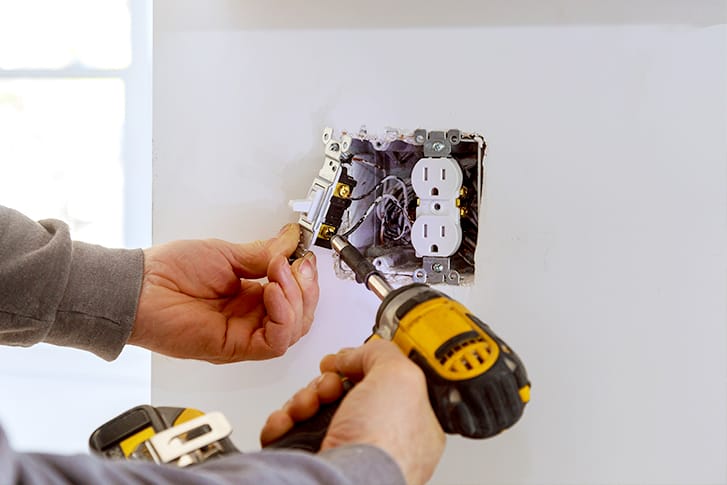 An electrician repairs an electrical wall outlet.